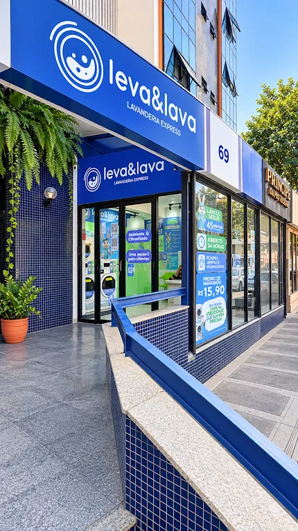 Entrada da Leva & Lava vista da calçada, com porta de vidro, o número 69 na fachada e aviso de ambiente climatizado