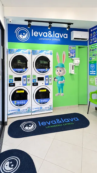 Interior da unidade com lavadoras e secadoras empilhadas e parede verde com o mascote da marca